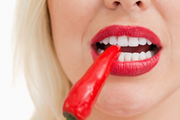Foto mulher loira mordendo uma pimenta vermelha