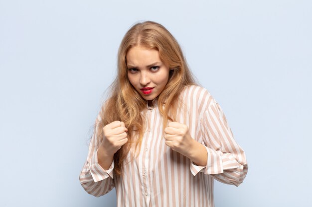 Mulher loira parecendo confiante, brava, forte e agressiva, com punhos prontos para lutar em posição de boxe