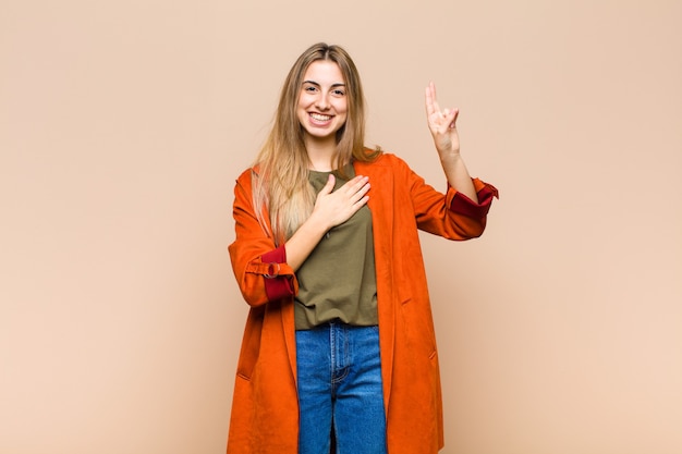 Mulher loira parecendo feliz, confiante e confiável, sorrindo e mostrando sinal de vitória, com uma atitude positiva