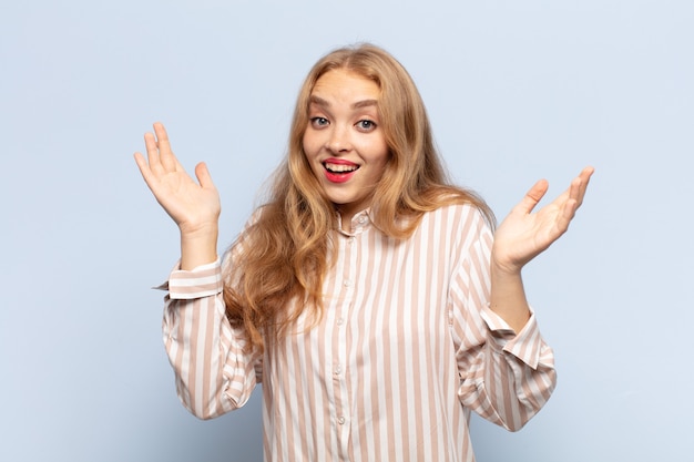 Mulher loira parecendo feliz e animada, chocada com uma surpresa inesperada com as duas mãos abertas ao lado do rosto