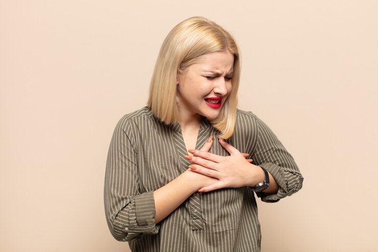 Foto mulher loira parecendo triste, magoada e com o coração partido, segurando as duas mãos perto do coração, chorando e se sentindo deprimida