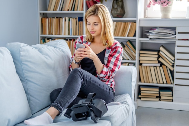 Mulher loira positiva relaxando em um sofá e usando dispositivo de óculos de realidade virtual