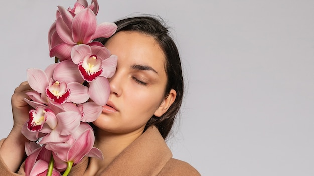 Mulher loira sedutora com jaqueta marrom posando no estúdio em background.elegant modelo cinza com roupa de primavera casual pastel. Linda garota com pele saudável e ramo de orquídea. Formato panorâmico 16: 9.