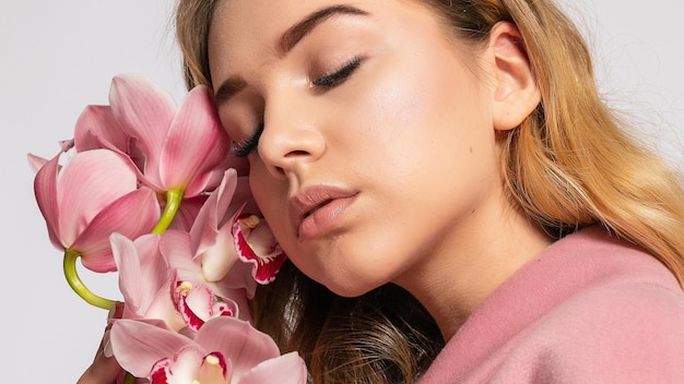 Mulher loira sedutora na jaqueta rosa posando no estúdio em fundo cinza modelo elegante em roupa de primavera casual pastel Linda garota com pele saudável e formato panorâmico de ramo orquídea 169