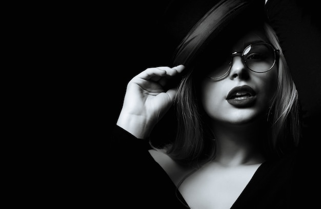 Mulher loira sedutora usa chapéu e óculos posando na sombra. Tonificação em preto e branco. Espaço para texto