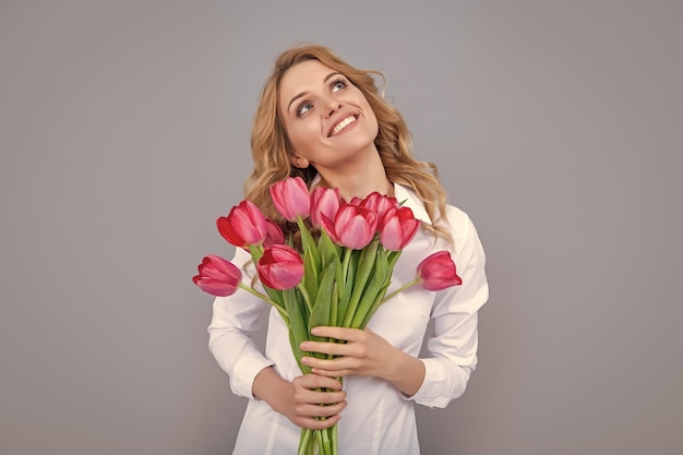 Mulher loira sonhadora com flores de tulipa de primavera em fundo cinza