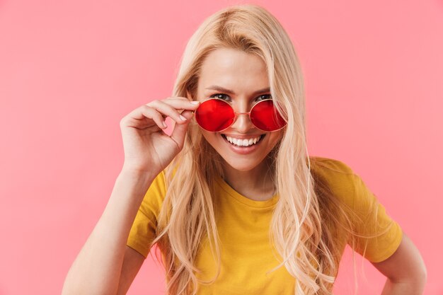 Mulher loira sorridente com óculos de sol sobre a parede rosa