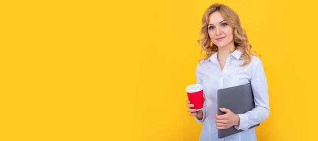 Mulher loira sorridente com uma xícara de café e computador em fundo amarelo Banner de retrato de rosto isolado de mulher com espaço de cópia simulado