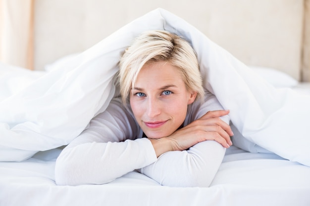 Mulher loira sorridente deitada na cama