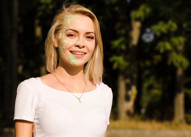 Mulher loira sorridente em uma camiseta branca com tinta colorida cobriu o rosto no Festival Holi