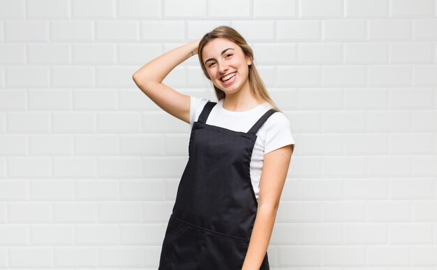 Foto mulher loira sorrindo alegre e casualmente, levando a mão na cabeça com um olhar positivo, feliz e confiante