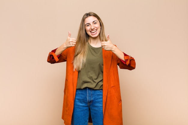 Mulher loira sorrindo alegremente e parecendo feliz, sentindo-se despreocupada e positiva com os dois polegares para cima