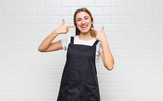 Mulher loira sorrindo com confiança apontando para seu próprio sorriso largo, atitude positiva, relaxada e satisfeita