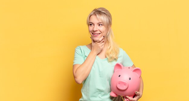 Mulher loira sorrindo com uma expressão feliz e confiante com a mão no queixo, pensando e olhando para o lado