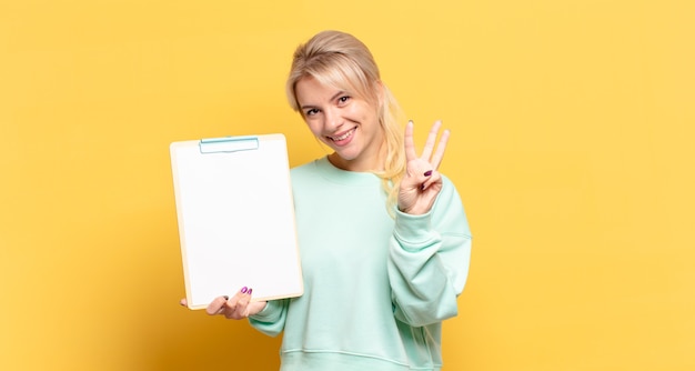 Mulher loira sorrindo e parecendo amigável, mostrando o número três ou terceiro com a mão para a frente, em contagem regressiva