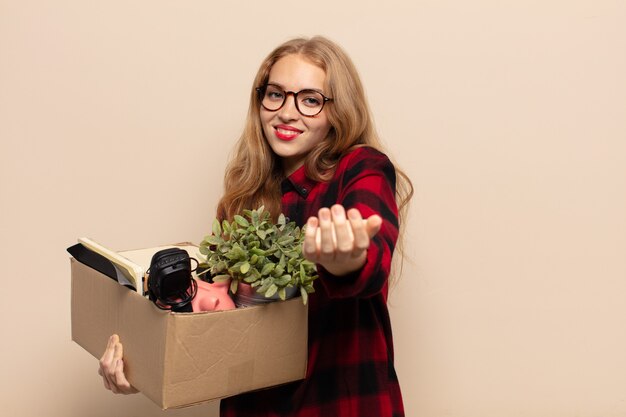 Mulher loira sorrindo feliz com um olhar amigável, confiante e positivo, oferecendo e mostrando um objeto ou conceito