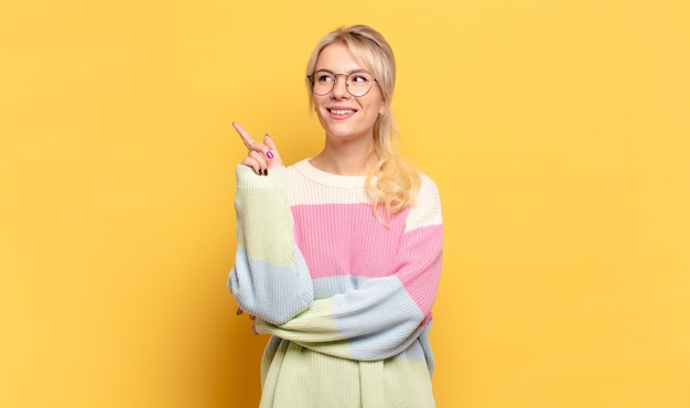 Mulher loira sorrindo feliz e olhando de soslaio, pensando, pensando ou tendo uma ideia