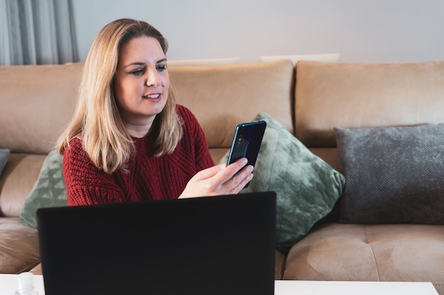 Foto mulher loira trabalhando em casa com laptop e smartphone