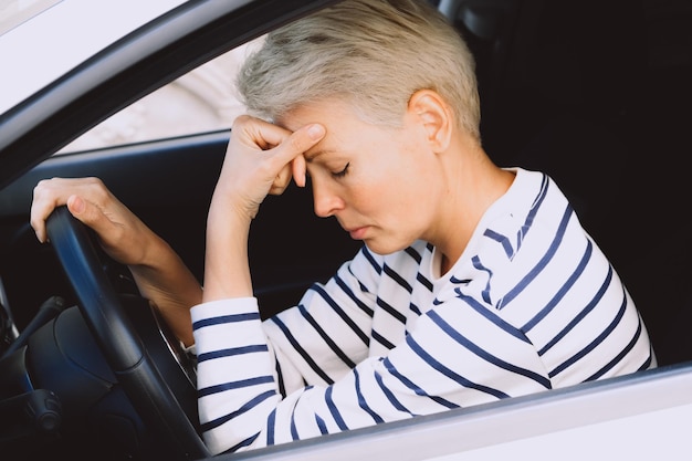 Mulher loira triste sentada em um carro branco e se sentindo deprimida