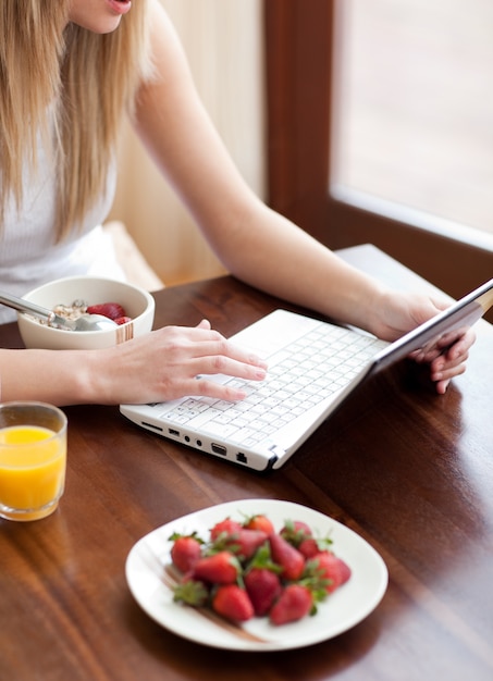 Mulher loira usando um laptop enquanto toma café da manhã