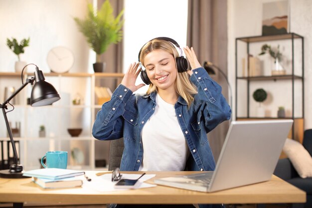 Mulher loira vestida com camisa jeans casual ouvindo meditação com fones de ouvido e dançando