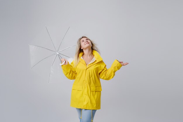 Foto mulher loira, vestindo capa de chuva amarela, segurando o guarda-chuva transparente, verificando o tempo se está chovendo