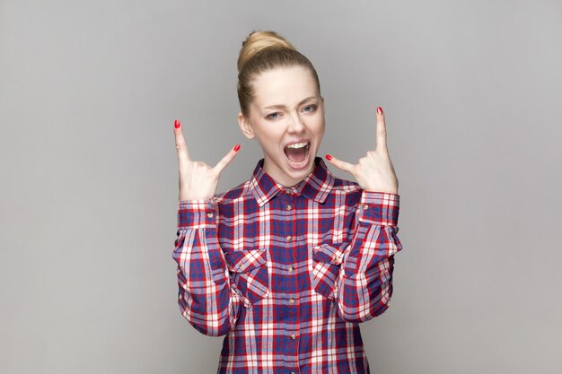 Foto mulher louca e excitada com penteado de pão de pé mostrando gesto de rock and roll gritando