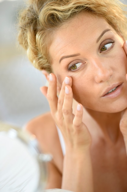 Foto mulher loura de meia idade que põe cosméticos sobre