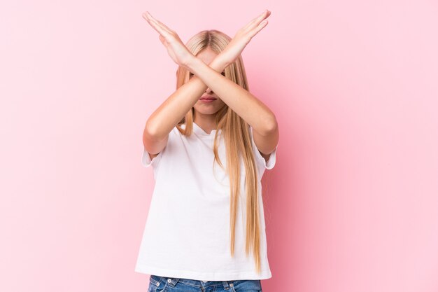 Mulher loura nova na parede cor-de-rosa que mantém dois braços cruzados, conceito da negação.