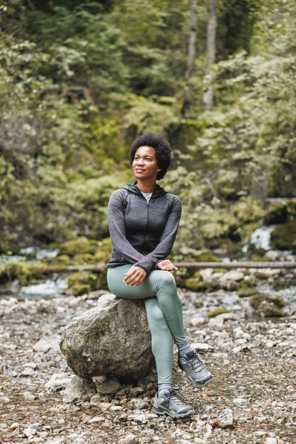 Mulher madura afro-americana vestindo roupas esportivas está se preparando para correr nas montanhas e desfrutar de treinamento ao ar livre.