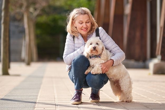 Mulher madura andando com cachorro branco fofo na cidade de verão.