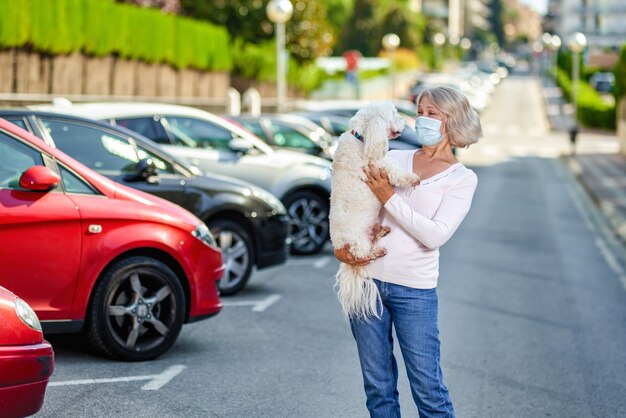 Mulher madura andando com um cachorro ao ar livre uma máscara antivírus.