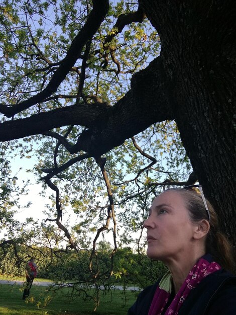 Foto mulher madura atenciosa olhando para longe enquanto está de pé perto de uma árvore no parque