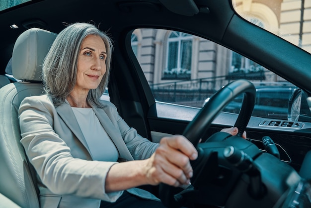 Mulher madura bonita em roupa casual inteligente sorrindo enquanto dirige o carro