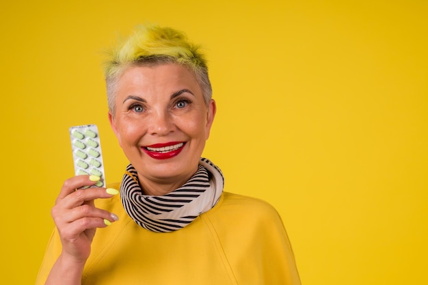 Mulher madura com cabelo tingido de amarelo estiloso e colorido em vestido quente segura pacote de pílulas em estúdio cópia de fundo