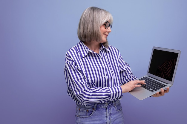 Mulher madura com cabelos grisalhos domina profissões remotas on-line usando um laptop em um estúdio brilhante