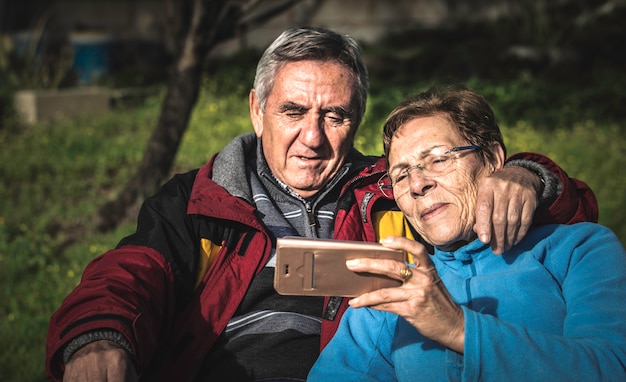 Mulher madura com o smartphone abraçado por seu marido quando ambos que sentam-se no parque.