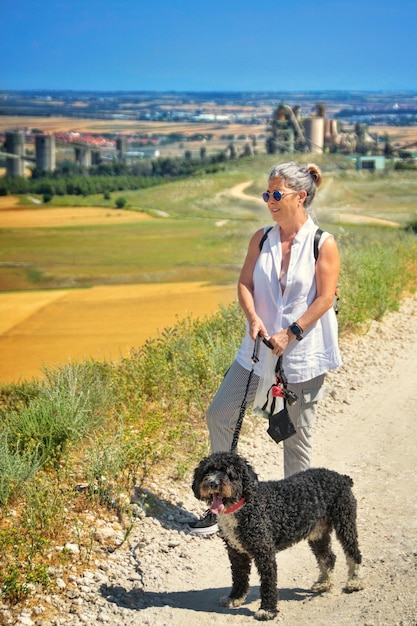 Mulher madura com óculos de sol posando no campo com um cão de água espanhol.