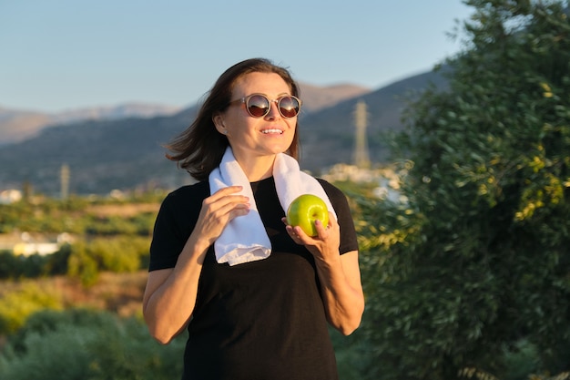 Mulher madura comendo maçã, estilo de vida saudável de mulheres, esporte e comida saudável, fundo de natureza do sol