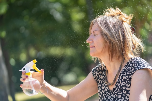 Mulher madura curvando-se em um parque público com um vaporizador de água no meio do verão