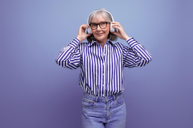 mulher madura de 60 anos com cabelos grisalhos a ouvir música com fones de ouvido num fundo de estúdio brilhante