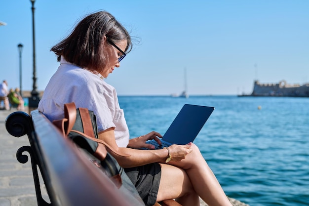 Mulher madura de negócios sentada ao ar livre usando laptop