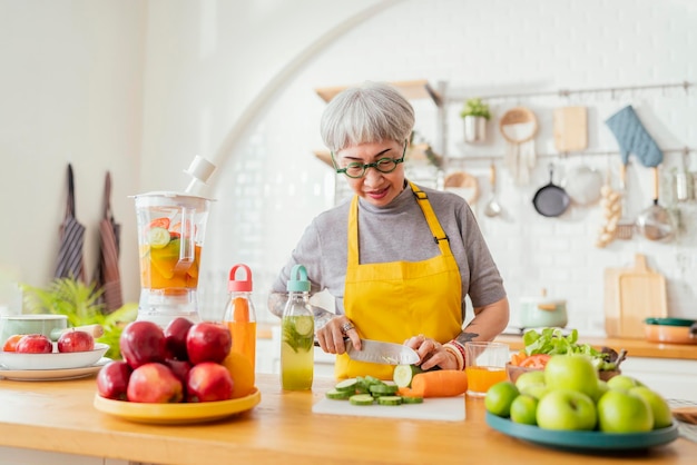 Foto mulher madura de tatuagem sorridente comendo salada de frutas e legumes mulher madura atraente com salada de frutas verdes frescas em casa avental de mulher sênior em pé no balcão da cozinha relaxando em casa