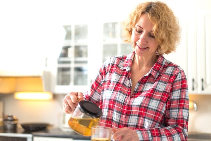 Foto mulher madura derramando chá em xícara na cozinha