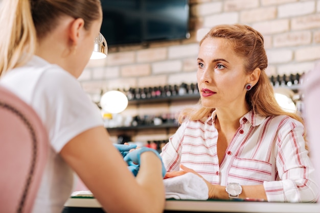 Mulher madura duvidosa conversando com manicure que cuida das unhas