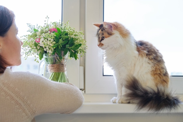 Mulher madura e gato tricolor doméstico sentado na janela