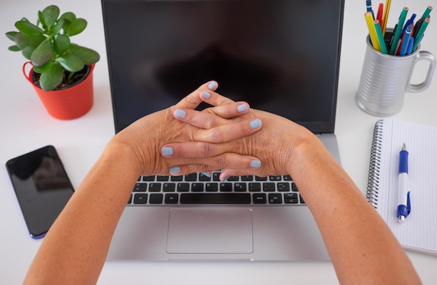 Mulher madura fazendo alongamento com as mãos depois de usar o laptop em casa.