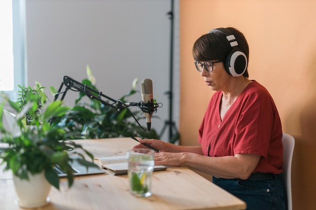 Mulher madura fazendo gravação de podcast para seu show online mulher de negócios atraente usando fones de ouvido