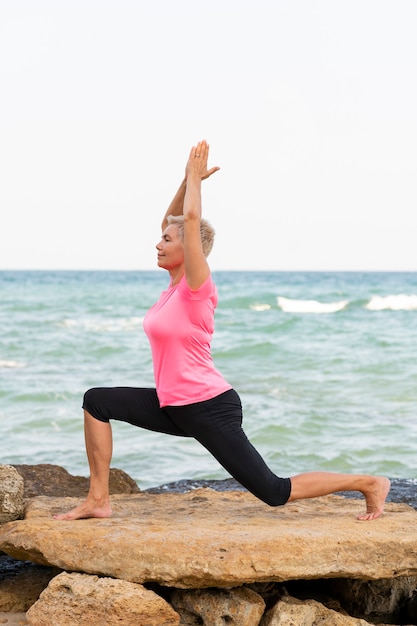 Mulher madura fazendo pilates à beira-mar. Retrato da vista lateral vertical. Foto de alta qualidade