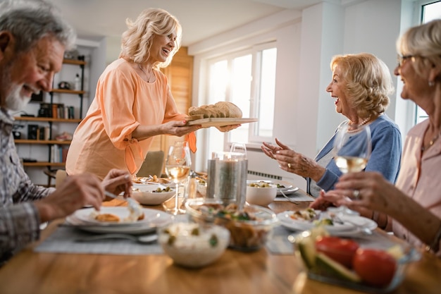 Mulher madura feliz almoçando com seus amigos e trazendo pão na mesa de jantar